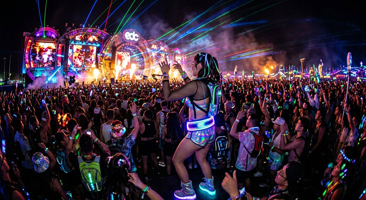 Festival-goer at EDC wearing an LED Glow Belt at night with massive crowd and stage lights